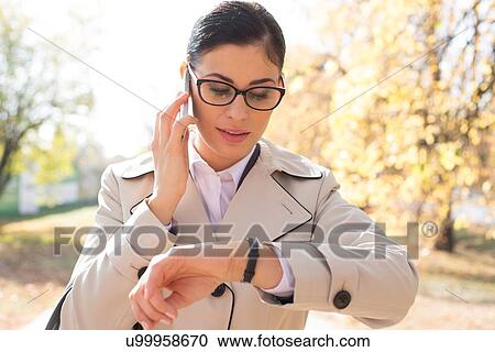 Businesswoman checking time while using smart phone at park View Large Photo Image Stock Image - Businesswoman checking time while using smart phone at park. Fotosearch