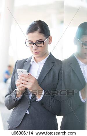 Businesswoman using cell phone while leaning on glass wall View Large Photo Image Picture - Businesswoman using cell phone while leaning on glass wall. Fotosearch