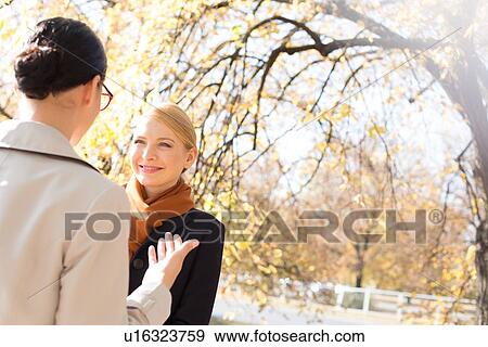 Stock Photo - Businesswomen conversing at park on sunny day. Fotosearch