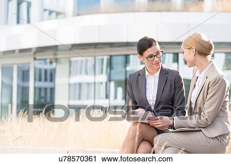 Businesswomen discussing over documents while sitting outside office building View Large Photo Image Stock Image - Businesswomen discussing over documents while sitting outside office building. Fotosearch