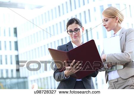 Stock Photo - Businesswomen reading folder while standing outside office building. Fotosearch