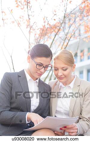 Businesswomen reading papers while sitting outdoors View Large Photo Image Stock Image - Businesswomen reading papers while sitting outdoors. Fotosearch