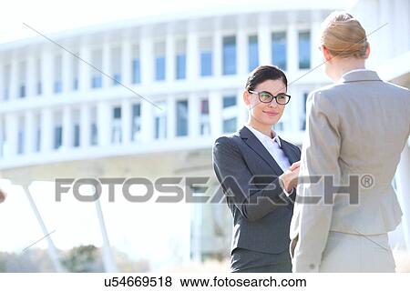 Businesswomen shaking hands outside office building View Large Photo Image Stock Photo - Businesswomen shaking hands outside office building. Fotosearch