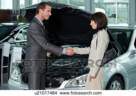 Car salesperson shaking hands with customer at showroom View Large Photo Image Picture - Car salesperson shaking hands with customer at showroom. Fotosearch