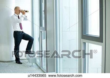 Stock Photography - caucasian businessman spying using telescope thru office window. Fotosearch