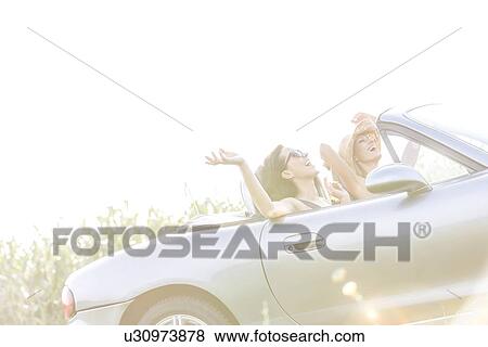 Cheerful female friends enjoying road trip in convertible on sunny day View Large Photo Image Stock Photo - Cheerful female friends enjoying road trip in convertible on sunny day. Fotosearch
