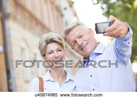 Cheerful middle-aged couple taking self portrait outdoors View Large Photo Image Stock Photography - Cheerful middle-aged couple taking self portrait outdoors. Fotosearch