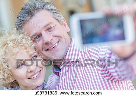 Close-up of happy middle-aged couple taking selfie through smart phone View Large Photo Image Stock Photograph - Close-up of happy middle-aged couple taking selfie through smart phone. Fotosearch