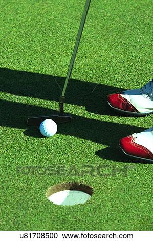 Stock Image - Close up of person putting golf ball on golf course. Fotosearch