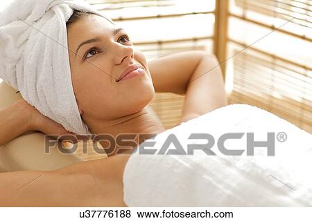 Stock Photo - Close-up of young woman relaxing on massage table with hands behind head. Fotosearch
