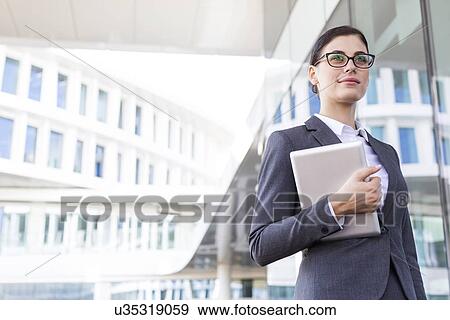 Stock Photo - Confident businesswoman holding tablet PC outside office building. Fotosearch