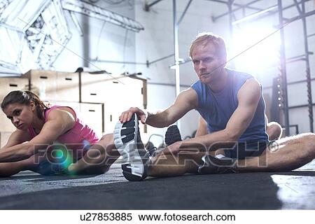 Stock Photography - Confident man and woman doing stretching exercise in crossfit gym. Fotosearch