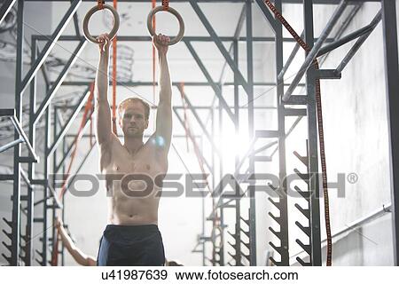 Stock Photo - Confident man exercising with gymnastic rings in crossfit gym. Fotosearch