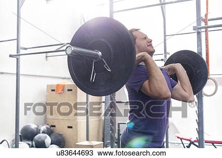 Confident man lifting barbell in crossfit gym View Large Photo Image Stock Image - Confident man lifting barbell in crossfit gym. Fotosearch
