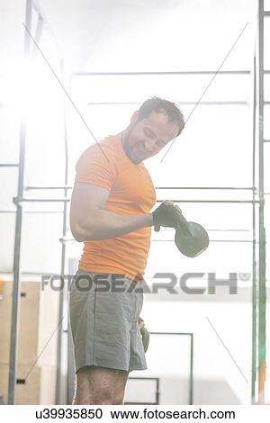 Confident man lifting kettlebell in crossfit gym View Large Photo Image Stock Image - Confident man lifting kettlebell in crossfit gym. Fotosearch