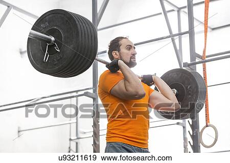 Stock Photo - Confident man looking away while lifting barbell in crossfit gym. Fotosearch