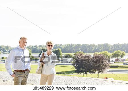Stock Photo - Confident middle-aged couple standing at park against clear sky. Fotosearch