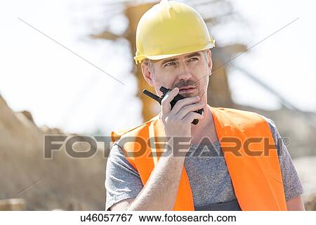 Confident supervisor using walkie-talkie at construction site View Large Photo Image Stock Photo - Confident supervisor using walkie-talkie at construction site. Fotosearch