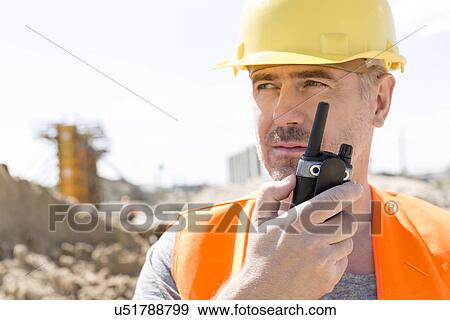Stock Photo - Confident supervisor using walkie-talkie at construction site. Fotosearch