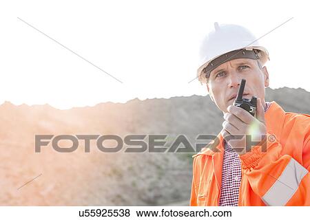 Stock Photo - Confident supervisor using walkie-talkie on construction site against clear sky. Fotosearch