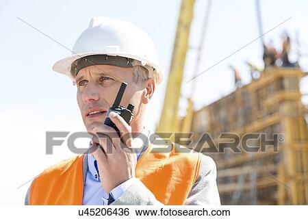 Confident supervisor using walkie-talkie at construction site View Large Photo Image Stock Photograph - Confident supervisor using walkie-talkie at construction site. Fotosearch