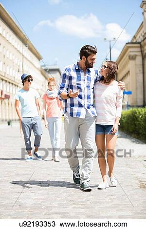 Couple walking on street with friends in background View Large Photo Image Stock Image - Couple walking on street with friends in background. Fotosearch