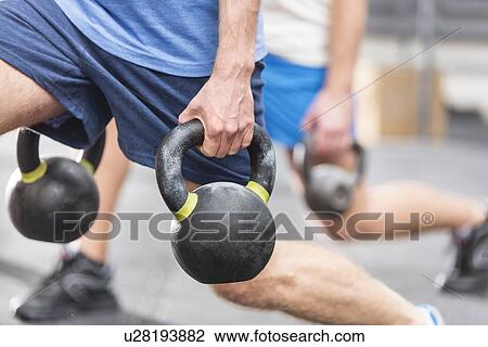 Stock Image - Cropped image of men lifting kettlebells at crossfit gym. Fotosearch