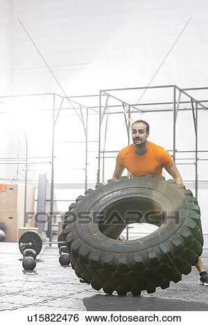 Stock Photograph - Dedicated man flipping tire in crossfit gym. Fotosearch