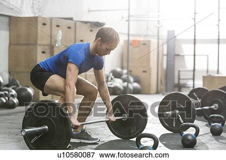 Stock Photo - Dedicated man lifting barbell in crossfit gym. Fotosearch
