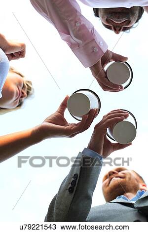 Stock Image - Directly below shot of businesspeople holding disposable cups against clear sky. Fotosearch