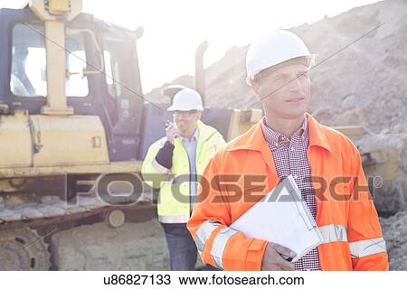 Engineer holding clipboard on construction site with colleague in background View Large Photo Image Stock Image - Engineer holding clipboard on construction site with colleague in background. Fotosearch