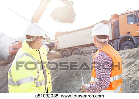 Engineer pointing at vehicles while discussing at construction site View Large Photo Image Stock Photography - Engineer pointing at vehicles while discussing at construction site. Fotosearch