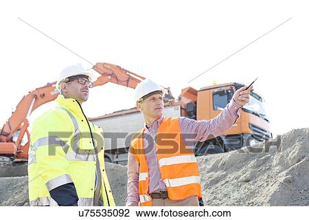 Engineer showing something to colleague while discussing at construction site against clear sky View Large Photo Image Stock Image - Engineer showing something to colleague while discussing at construction site against clear sky. Fotosearch