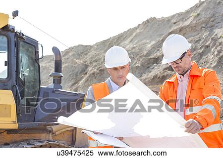 Stock Photography - Engineers analyzing blueprint at construction site. Fotosearch