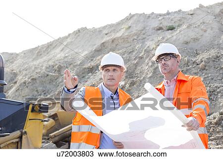 Engineers discussing over blueprint at construction site View Large Photo Image Stock Image - Engineers discussing over blueprint at construction site. Fotosearch