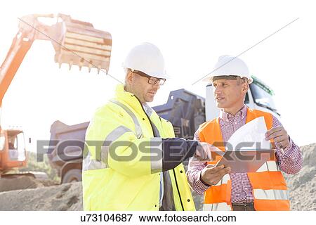 Engineers discussing over documents at construction site View Large Photo Image Stock Photo - Engineers discussing over documents at construction site. Fotosearch
