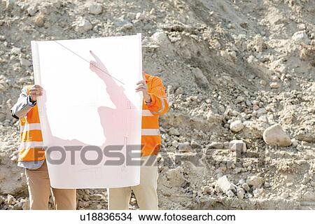 Picture - Engineers examining blueprint at construction site. Fotosearch