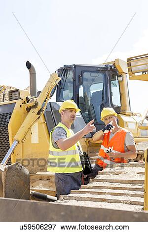 Stock Photo - Engineers pointing while discussing at construction site against clear sky. Fotosearch
