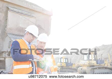 Stock Photography - Engineers using laptop at construction site against clear sky. Fotosearch