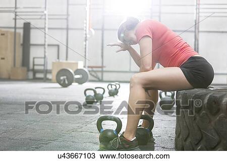 Stock Image - Exhausted woman sitting on tire in crossfit gym. Fotosearch