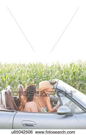 Stock Photograph - Female friends reading map in convertible against clear sky. Fotosearch
