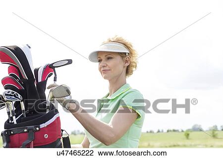 Stock Image - Female golfer with golf club bag against clear sky. Fotosearch