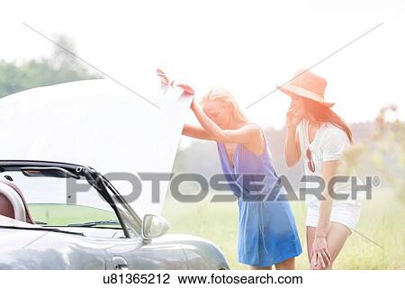 Stock Image - Friends examining broken down car on sunny day. Fotosearch