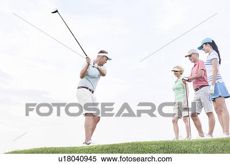 Friends looking at man playing golf against sky View Large Photo Image Stock Photography - Friends looking at man playing golf against sky. Fotosearch