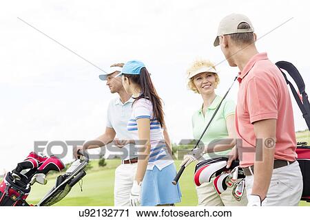 Stock Image - Friends talking while walking at golf course against clear sky. Fotosearch