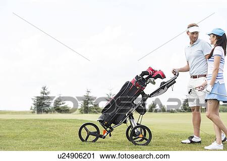 Friends with equipment talking while walking at golf course against clear sky View Large Photo Image Stock Image - Friends with equipment talking while walking at golf course against clear sky. Fotosearch