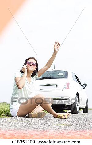 Frustrated woman hitchhiking while using cell phone by broken down car View Large Photo Image Stock Photo - Frustrated woman hitchhiking while using cell phone by broken down car. Fotosearch