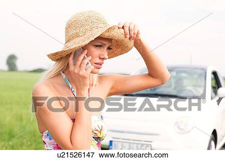 Stock Photo - Frustrated woman using cell phone by broken down car. Fotosearch