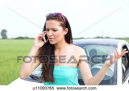 Stock Photography - Frustrated woman using cell phone against broken down car. Fotosearch