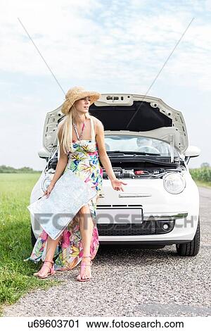 Stock Image - Frustrated woman with map sitting on broken down car. Fotosearch